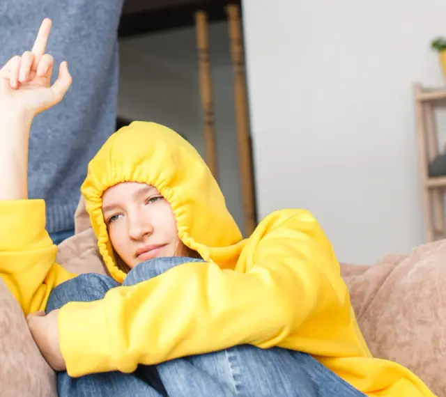Ein Teenager in gelbem Hoodie zeigt seiner Mutter den Mittelfinger. Er hat keinen Respekt vor ihr.