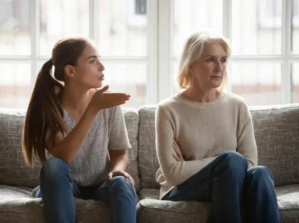 Junge Frau gestikuliert wütend, während ihre Mutter abgewandt sitzt. Es scheint, als ob meine Tochter mich hasst.