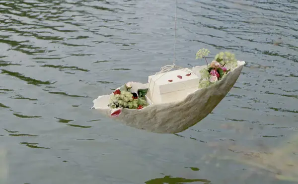 Ein Schiffchen mit Blumen und einer Schachtel schwimmt auf dem Wasser. Eine würdevolle Idee für Kinderbeerdigungen.