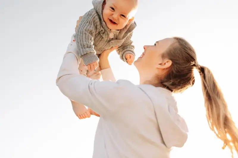 Mutter wirft ihr lachendes Baby in die Luft. Ein fröhlicher helikopter-mutter test im Freien.