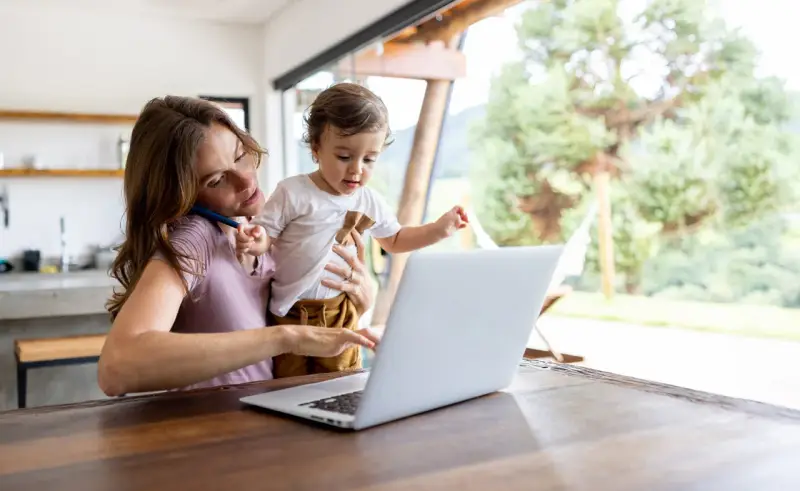 Als alleinerziehende Mutter jongliert sie Arbeit und Kind. Sie telefoniert, während sie ihr Kleinkind hält und am Laptop tippt.