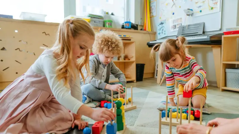 Drei Kinder, darunter ein **kind 8 jahre**, spielen konzentriert mit bunten Holzbausteinen im Kindergarten.