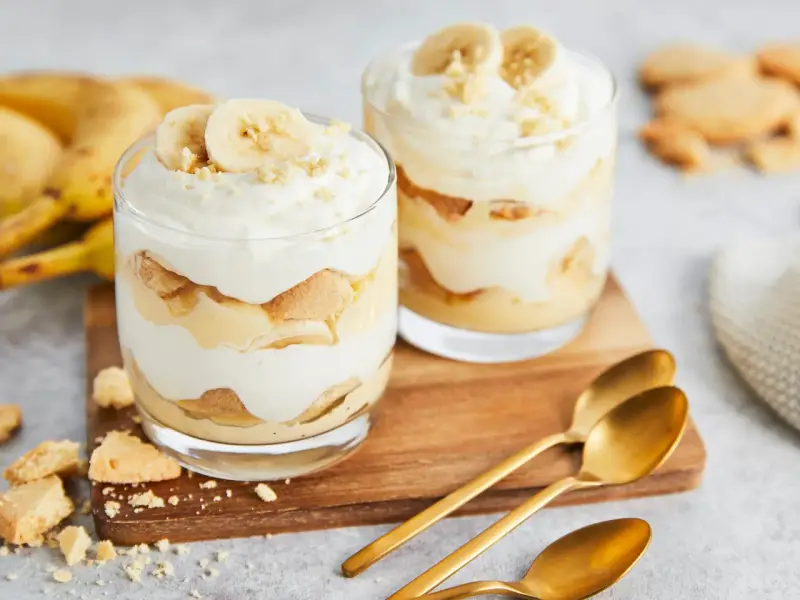 Zwei Gläser mit cremigem Bananenpudding, geschichtet mit Keksen und Bananenscheiben. Ein köstliches Bananenpudding Rezept zum Nachmachen.