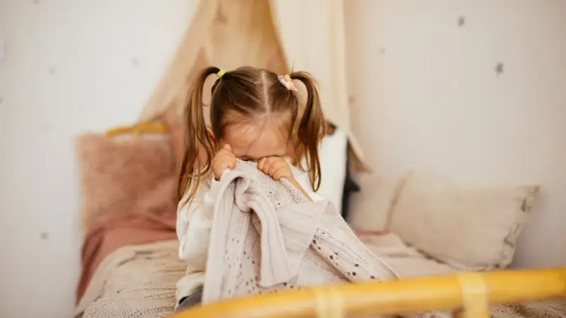 Kleines Kind mit Zöpfen versteckt sich unter einer Decke, weil es Angst vor Monstern hat.